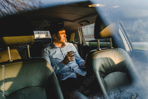 One man young adult male sitting on the back sit of the car wearing shirt holding a cup with coffee or drink looking to the side businessman manager going to work real people copy space