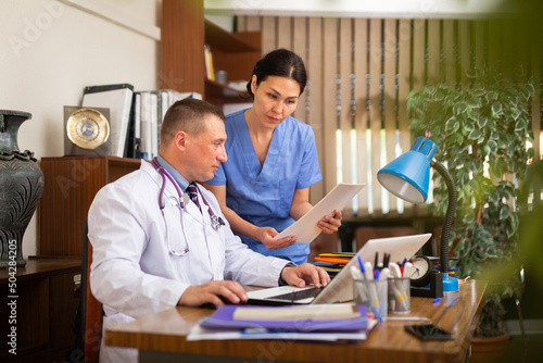 Two doctors man and woman analysing and consulting over medical record in modern hospital