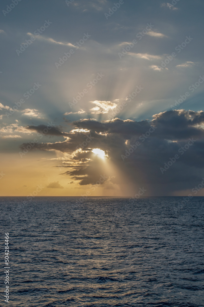 Sunset over the ocean with sunlight beaming through the clouds.