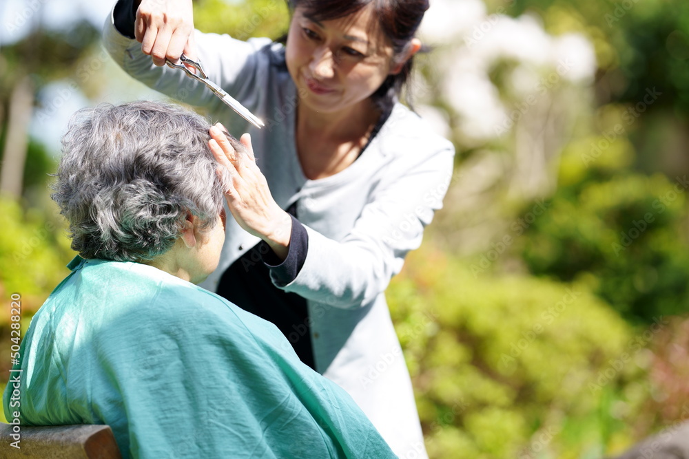 Fototapeta premium 庭でヘアカットしてもらう高齢女性
