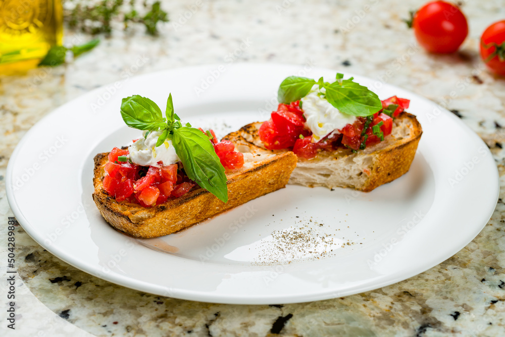 bruschetta with tomatoes and cheese strachatella with basil on white plate on marble table