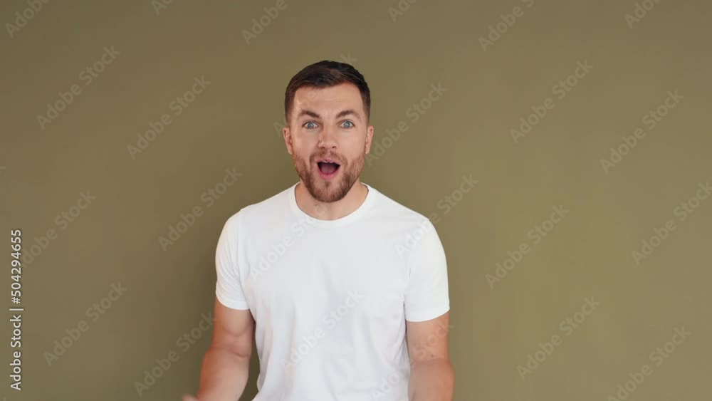 Against background. Man in casual clothes standing in the studio and showing emotions Against background. Man in casual clothes standing in the studio and showing emotions