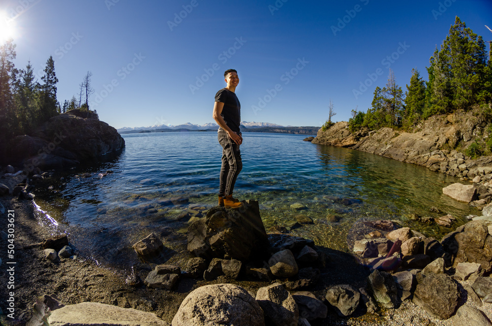 HOMBRE SOBRE UNA PIEDRA DE UN LAGO TRASPARENTE MIRANDO EL PAISAJE RODEADO DE montañaS HOMBRE SOBRE UNA PIEDRA DE UN LAGO TRASPARENTE MIRANDO EL PAISAJE RODEADO DE montañaS