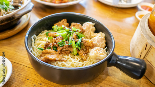 Egg noodle with stir fried garlic pork, a close up of Thai dry noodles on woodle table at Thai food restaurant background in Bangkok, Thailand