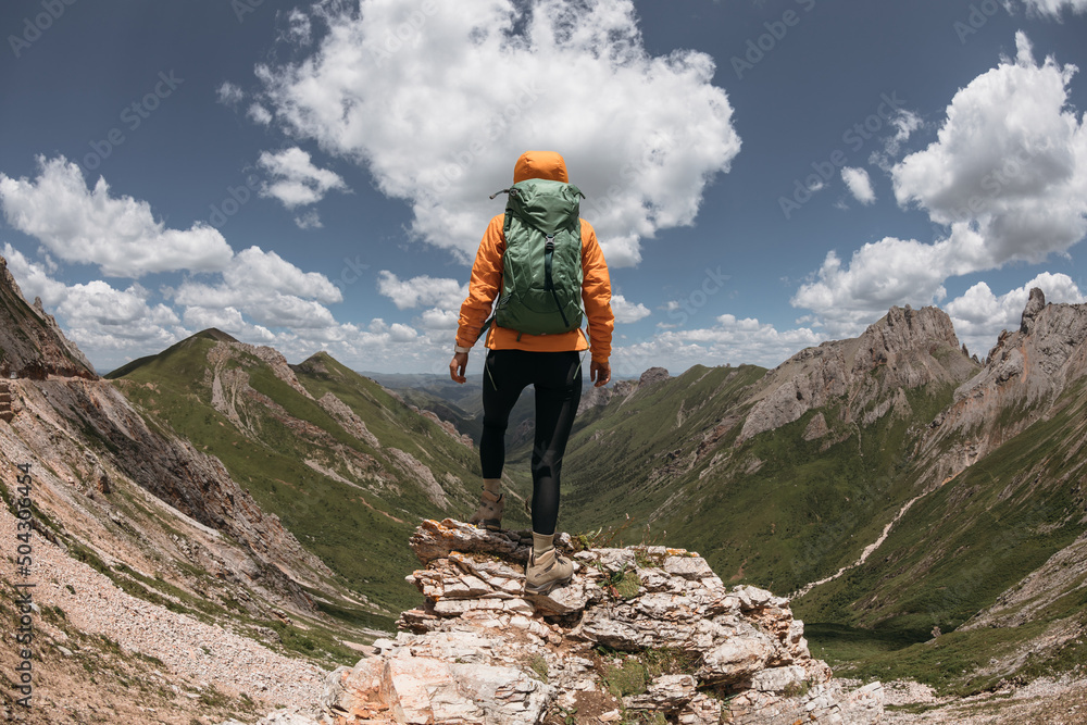 Successful woman backpacker hiking on sunset alpine mountain peak