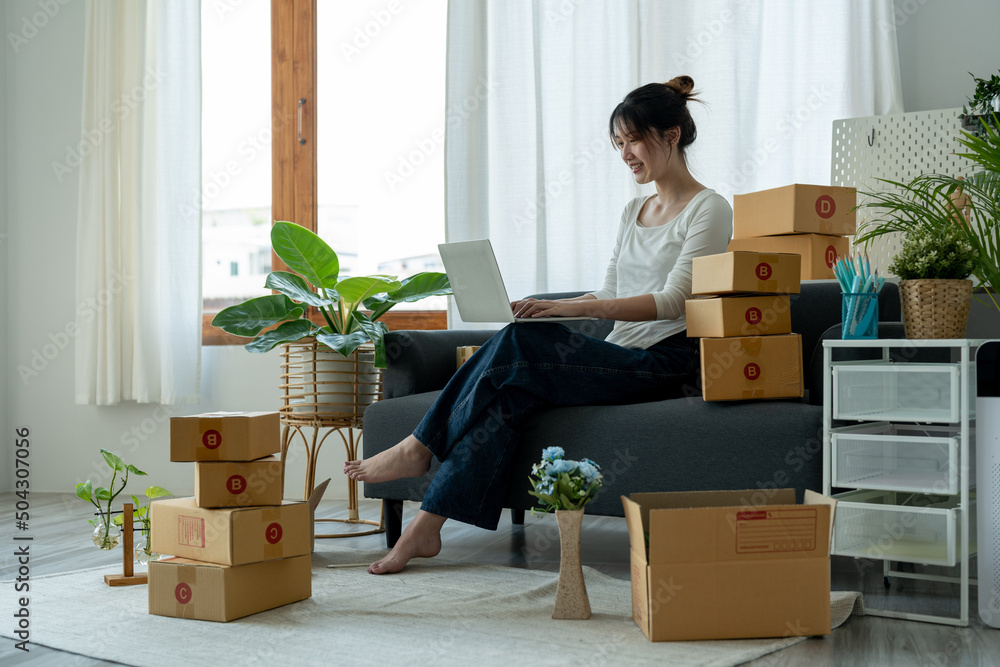 Startup small business owner working with computer at workplace. Freelance woman seller checking orders from laptop. Packing goods for delivery to customer. Online selling. E-commerce Startup small business owner working with computer at workplace. Freelance woman seller checking orders from laptop. Packing goods for delivery to customer. Online selling. E-commerce