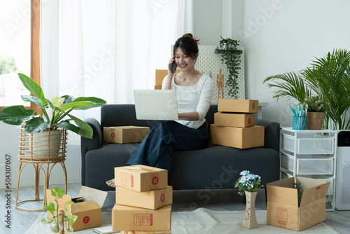 Startup small business owner working with computer at workplace. Freelance woman seller call confirm orders. Packing goods for delivery to customer. Online selling. E-commerce