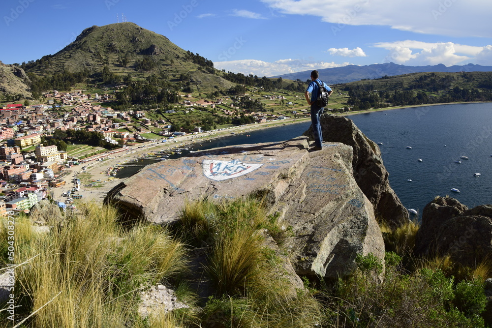 A man on a hilltop looks at the landscape of Copacabana and Lake Titicaca. Copacabana, Bolivia