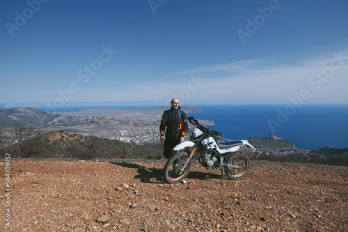 Active elderly man resting during offroad enduro dirt motorcycle trip in beautiful mountains hills and sea landscape