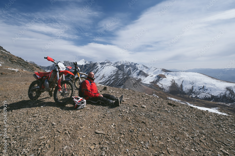 Portrait of 60-year-old Active man with grey hair resting near enduro motorcycle in beautiful snow mountain landscape Portrait of 60-year-old Active man with grey hair resting near enduro motorcycle in beautiful snow mountain landscape