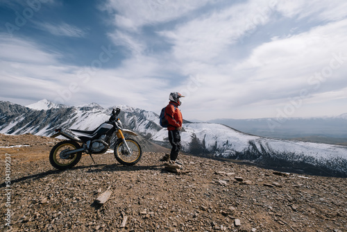 Active man resting near dirt bike looking on beautiful snow mountain landscape