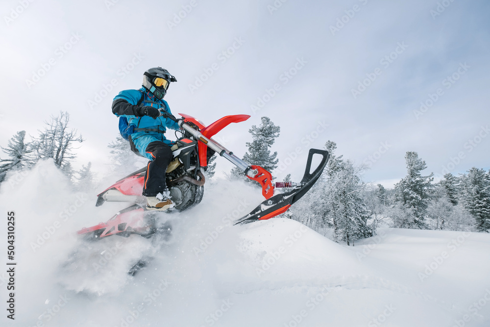 Motorcyclist jumping on snowbike in snow splashes in deep snow dust on winter day
