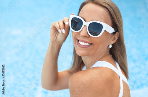 Closeup beautiful smiling woman in white trendy sunglasses relaxing by the swimming pool in a hotel on vacation © Evgeniya Grande