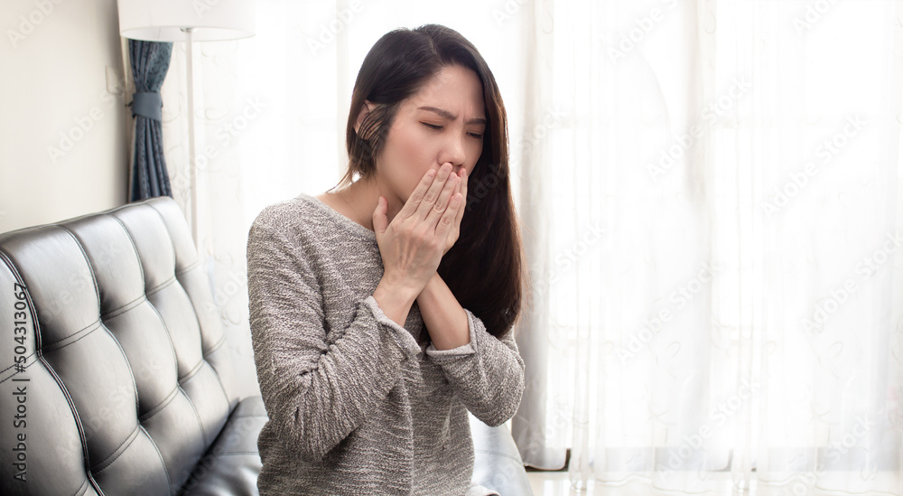 Asian beautiful woman are sitting on sofa in living room and coughing. Sick and a healthy concept Asian beautiful woman are sitting on sofa in living room and coughing. Sick and a healthy concept