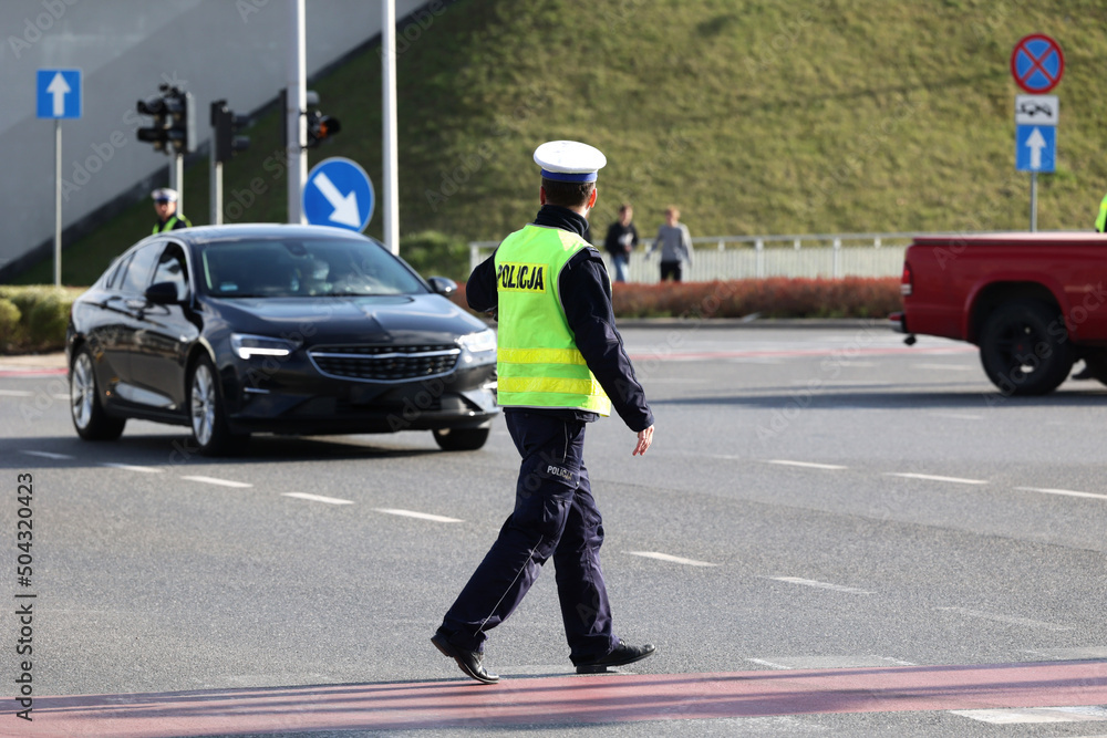 Policjant policji drogowej podczas nadzoru ruchu drogowego z radiowozem.  - obrazy, fototapety, plakaty 