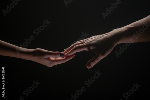 Two hands stretch each other, black background. Couple in love holding hads, close up. Helping hand, support, friendship.