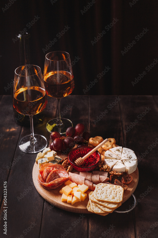 Sausage and cheese cut on round board with fruit, cookies and sauce with two glasses of white port and a bottle
