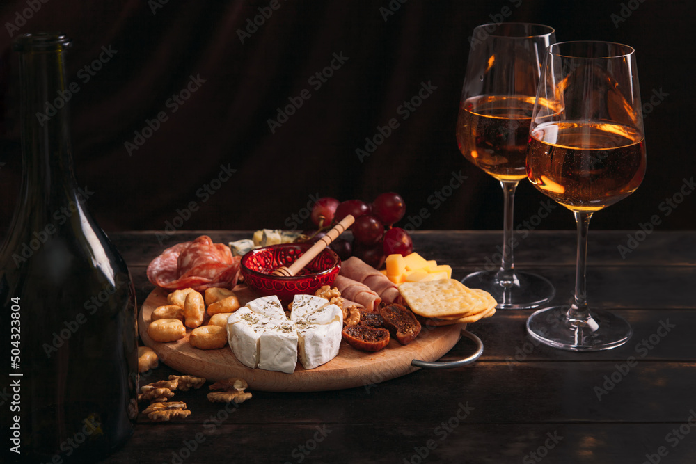 Sausage and cheese cut on round board with fruit, cookies and sauce with two glasses of white port and a bottle