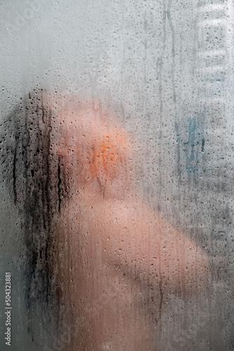 woman in shower view through glass covered with drops