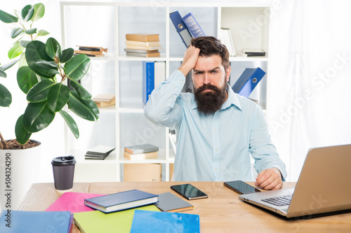 Frustated professional guy clutching head working at office desk, frustration photo