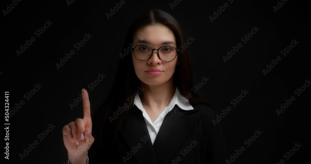 No sign gesture. Portrait of serious young businesswoman raising forefinger up saying no. A brunette with long hair wearing glasses and business clothes does not agree. Isolated on a black background No sign gesture. Portrait of serious young businesswoman raising forefinger up saying no. A brunette with long hair wearing glasses and business clothes does not agree. Isolated on a black background
