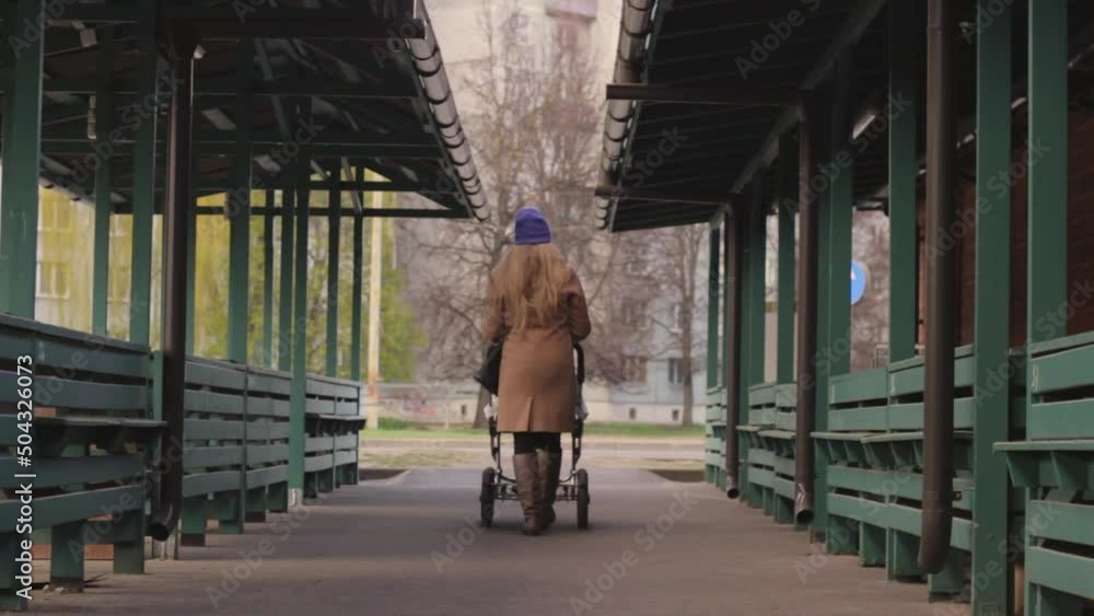 Lonely woman walking through empty market while pushing baby stroller, back zoom out view Lonely woman walking through empty market while pushing baby stroller, back zoom out view