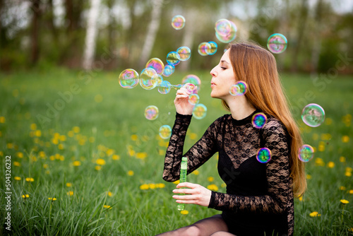 Pregnant girl in the spring in the grass blows soap bubbles. Copy space