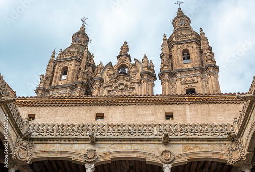 Parte alta del patio de estilo gótico de la casa de las conchas y sobresaliendo las torres barrocas de la iglesia La Clerencia en Salamanca, España