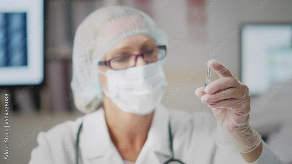 Medical worker in safety gloves, mask and cap holding ampoule with vaccine. Realtime Medical worker in safety gloves, mask and cap holding ampoule with vaccine. Realtime