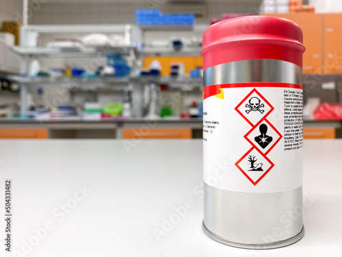 Can with extremely dangerous substance inside, labelled with symbols indicating that the content is toxic. Laboratory space is visible in the background. photo