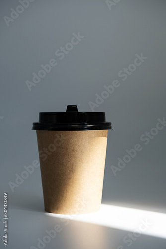 Mock up disposable craft cardboard takeaway coffee cup in light beam. Template to go coffee cup against grey background.