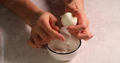 Woman hand peeling boiled egg in bowl