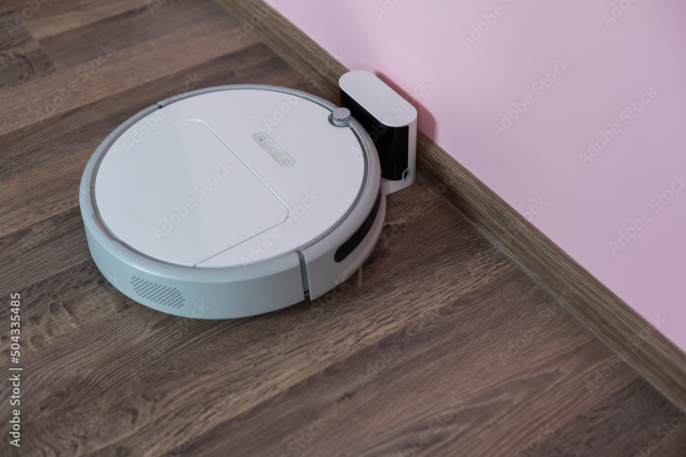 Foto Stock Robotic vacuum cleaner on laminate wood floor charging from base  station. Smart cleaning technology. robot vacuum cleaner return to charging  at dock in clean room floor | Adobe Stock