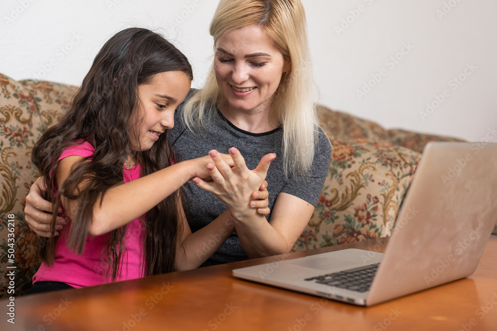 Cheerful toothy smiling happy mother and her little curious daughter are lying on a floor at home and usinf a laptop for watching cartoons, a girl is indicating on the monitor at the weekend. Cheerful toothy smiling happy mother and her little curious daughter are lying on a floor at home and usinf a laptop for watching cartoons, a girl is indicating on the monitor at the weekend.