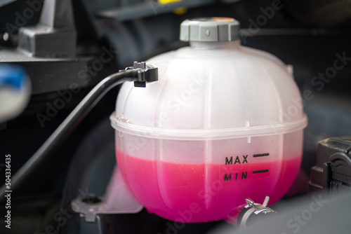 A car's engine coolant water supply box filled with pink color antifreeze liquid. Transportation equipment object photo. photo