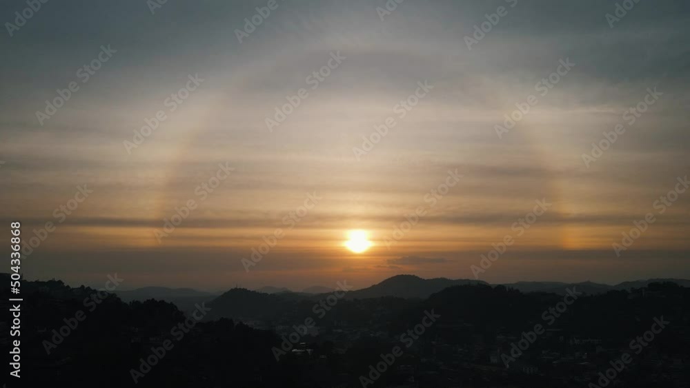 Beautiful setting sun with a rainbow circle between the thin veil clouds above the silhouettes of the mountains from the nature of Sri Lanka near Kandy. High level drone shot Beautiful setting sun with a rainbow circle between the thin veil clouds above the silhouettes of the mountains from the nature of Sri Lanka near Kandy. High level drone shot
