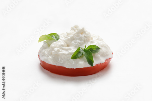 Stracciatella cheese on white background with basil on piece of tomato. Curd cheese product.