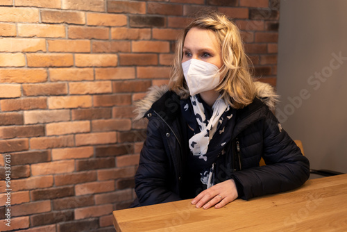 Frau mit FFP2 Maske sitzt an Tisch vor Backstein-Ziegelwand photo