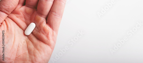 A man holds a white pill in the palm of his hand, close-up