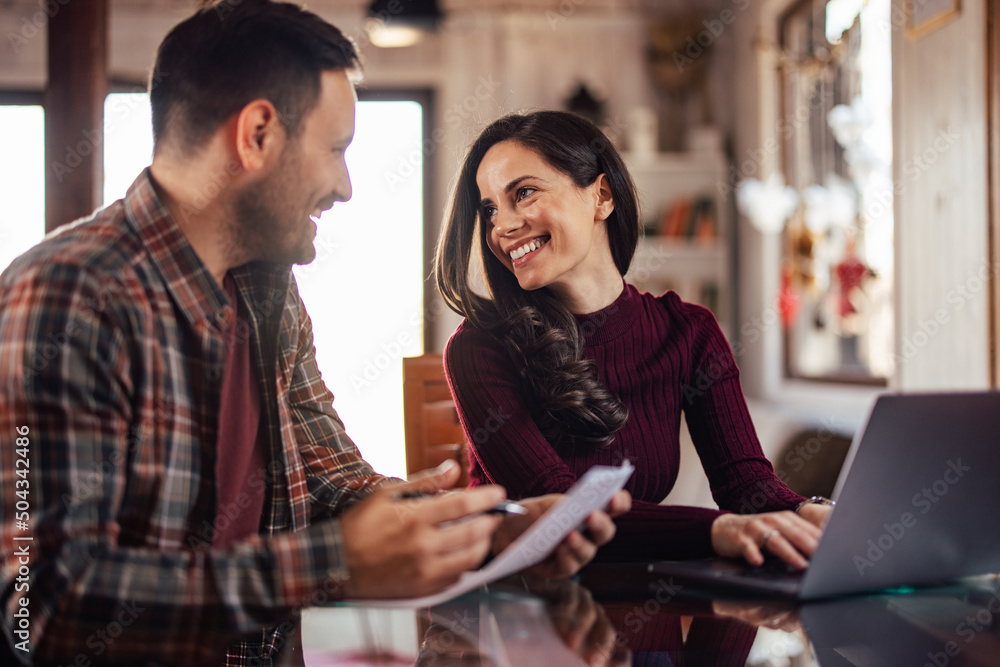 The smiling business couple, working from home, using a laptop and holding some documents. The smiling business couple, working from home, using a laptop and holding some documents.