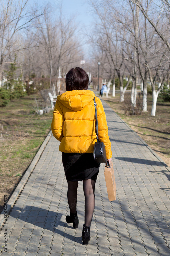 A woman bright yellow jacket walks through the streets of the city in spring.