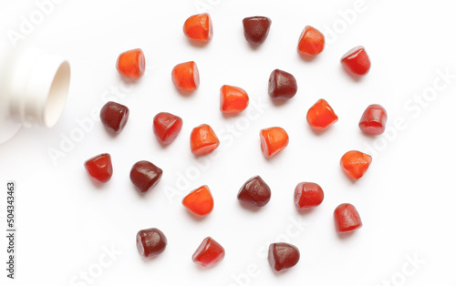 Group of red, orange and purple multivitamin gummies with the bottle isolated on white background. 