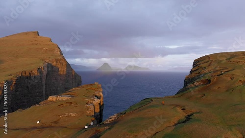 Aerial view of golden expanse of land during sunset. Background of cliff in Faroe Island, blue sea and islands in a suggestive drone video. photo