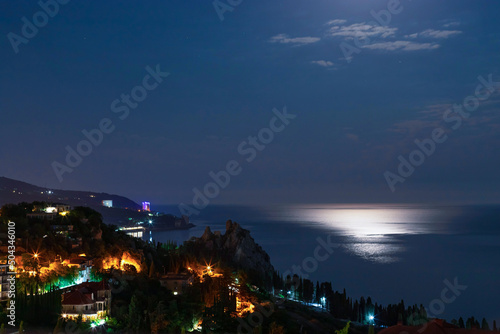 Night view of cityscape on coast of mediterranean sea with lights illumination. dark blue sky and calm sea.