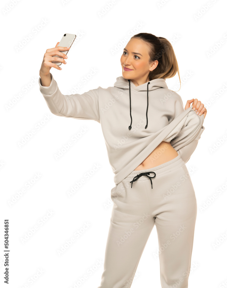 Beautiful young woman in tracksuit taking a selfie in the white studio background Beautiful young woman in tracksuit taking a selfie in the white studio background