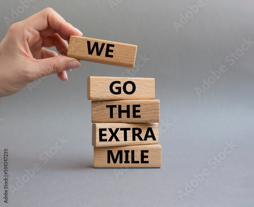 We go the extra mile symbol. Wooden blocks with words 'We go the extra mile'. Beautiful grey background. Businessman hand. Business and 'We go the extra mile' concept. Copy space. photo