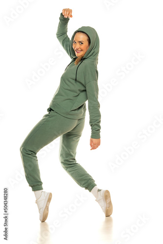 a young woman in a green tracksuit and hood, poses against a white background in the studio