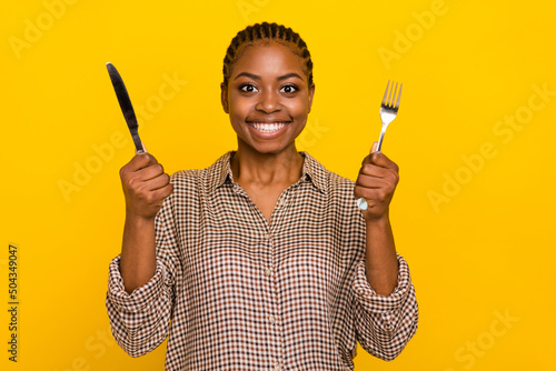 Photo of positive funny lady dressed checkered shirt holding silver fork knife isolated yellow color background photo