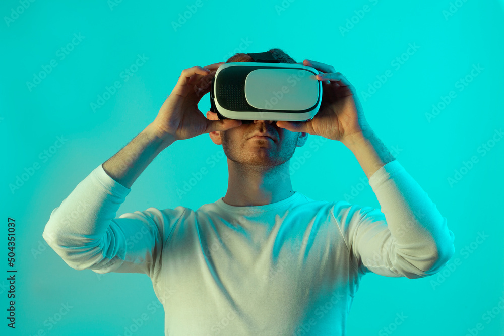 Modern young man experiencing virtual reality glasses in futuristic neon illuminated studio Modern young man experiencing virtual reality glasses in futuristic neon illuminated studio