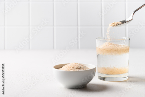Billede på lærred Woman adds psyllium fiber to glass of water on white background